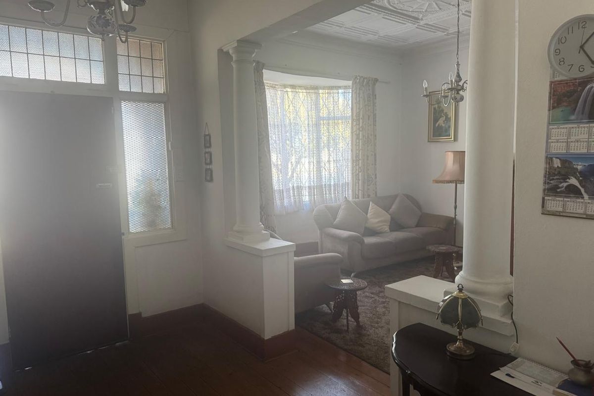 A character-filled living room featuring original pressed metal ceilings, decorative ceiling roses, classical columns, and polished timber flooring with a bay window.