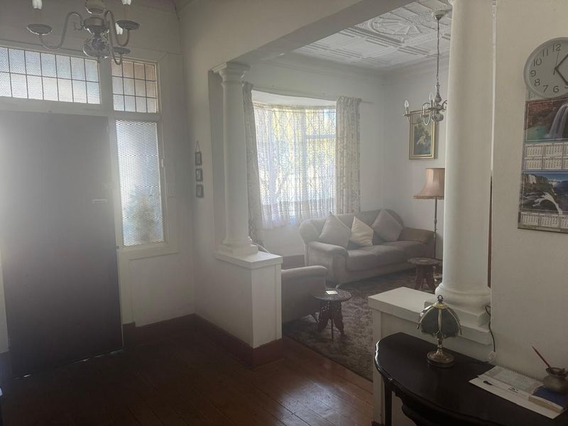 A character-filled living room featuring original pressed metal ceilings, decorative ceiling roses, classical columns, and polished timber flooring with a bay window.