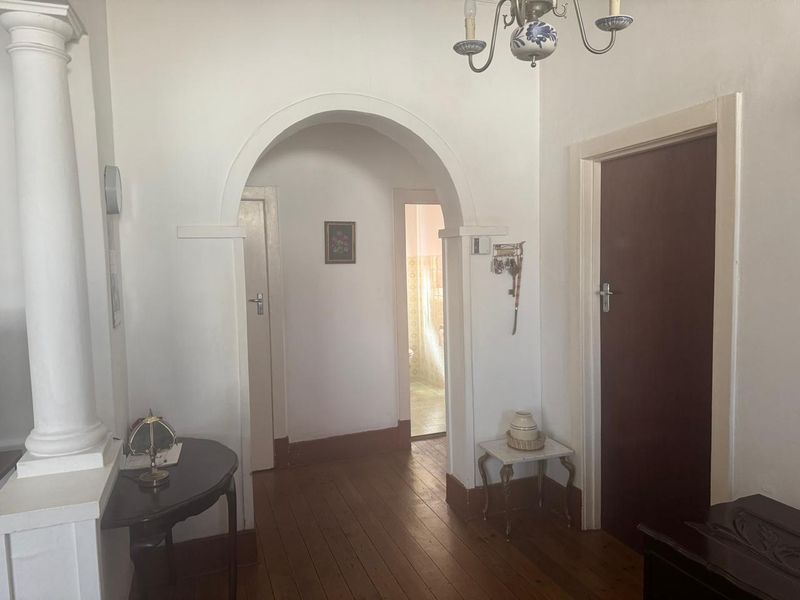 A traditional hallway featuring hardwood flooring, an arched entryway, and classic architectural details connecting multiple rooms.