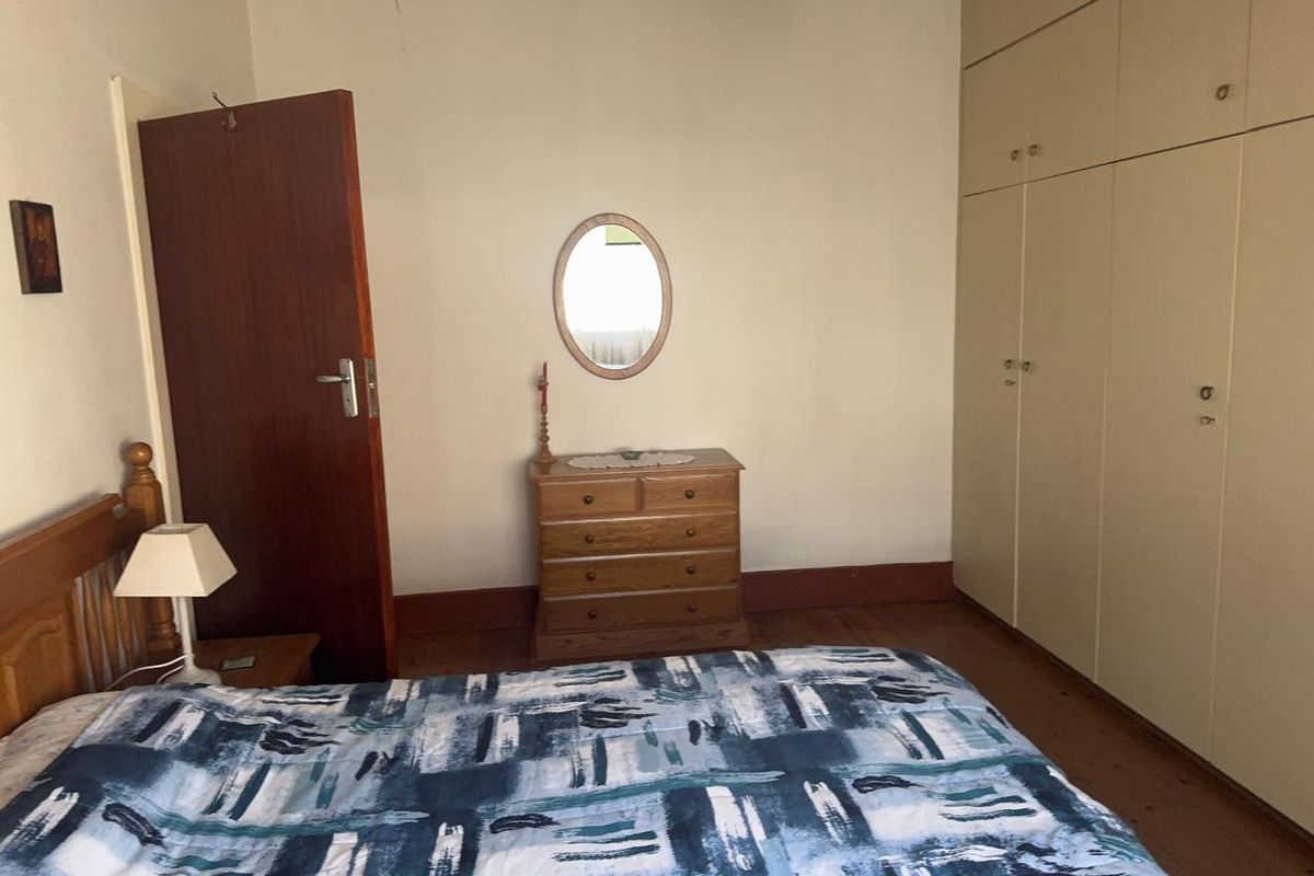 A bedroom featuring built-in cupboards and timber flooring, offering a functional space with potential for cosmetic updates.