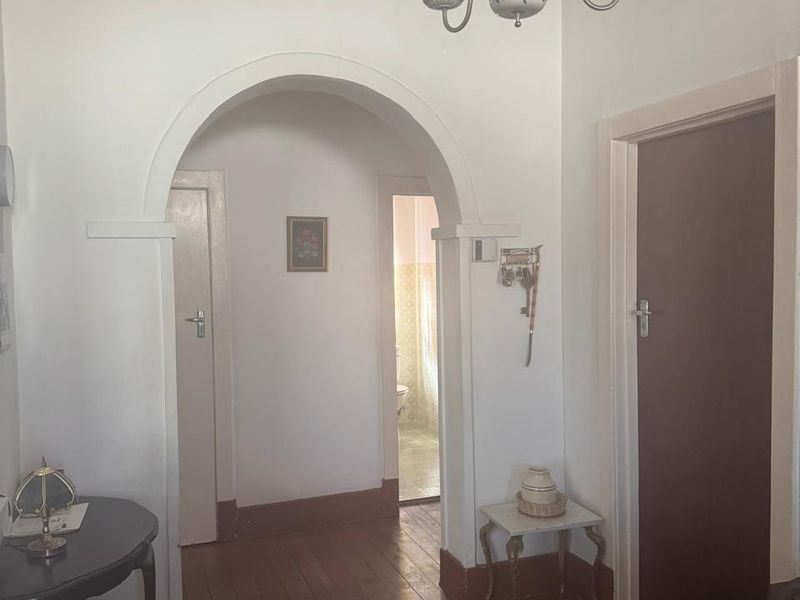 A classic hallway featuring original timber flooring, a decorative ceiling rose, and a distinctive archway leading to adjacent rooms.