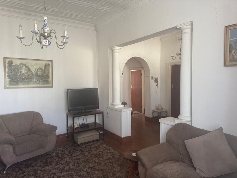 A traditional living room featuring decorative ceiling tiles, classical columns, an archway, and hardwood flooring, offering a character-filled space with potential for modernization.