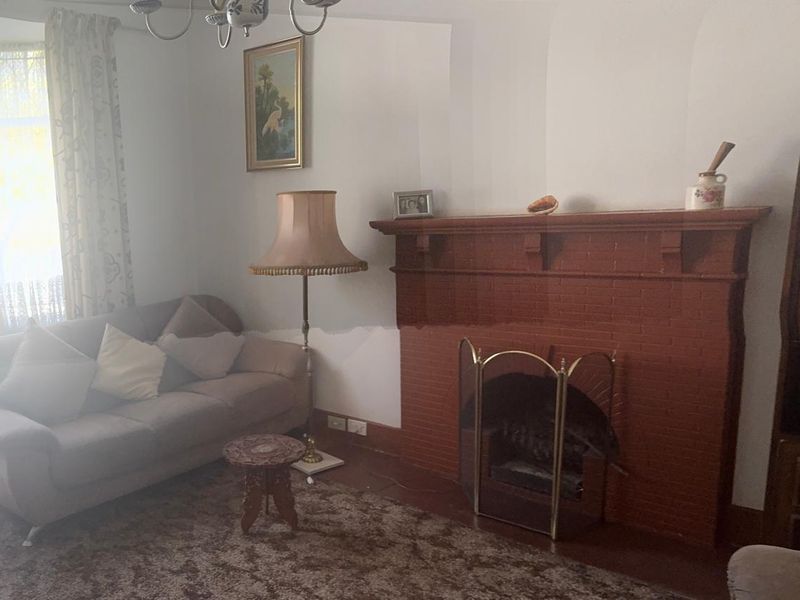 A traditional living room featuring a prominent brick fireplace with a timber mantelpiece and coved ceiling details.