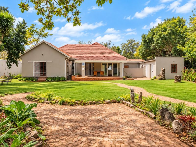 Rear view of the house featuring a well-maintained garden, brick paved pathways, and a covered patio area under a terracotta tiled roof.