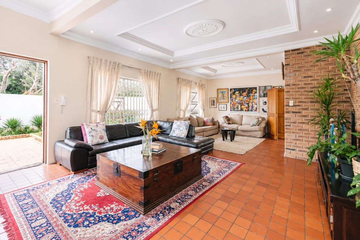Spacious living room featuring terracotta tile flooring, an exposed brick feature wall, and a decorative tray ceiling with recessed lighting.
