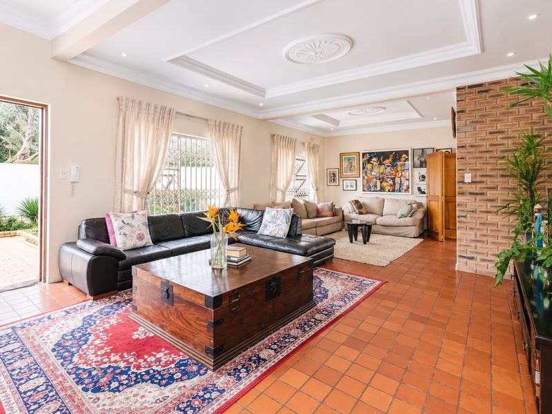 Spacious living room featuring terracotta tile flooring, an exposed brick feature wall, and a decorative tray ceiling with recessed lighting.