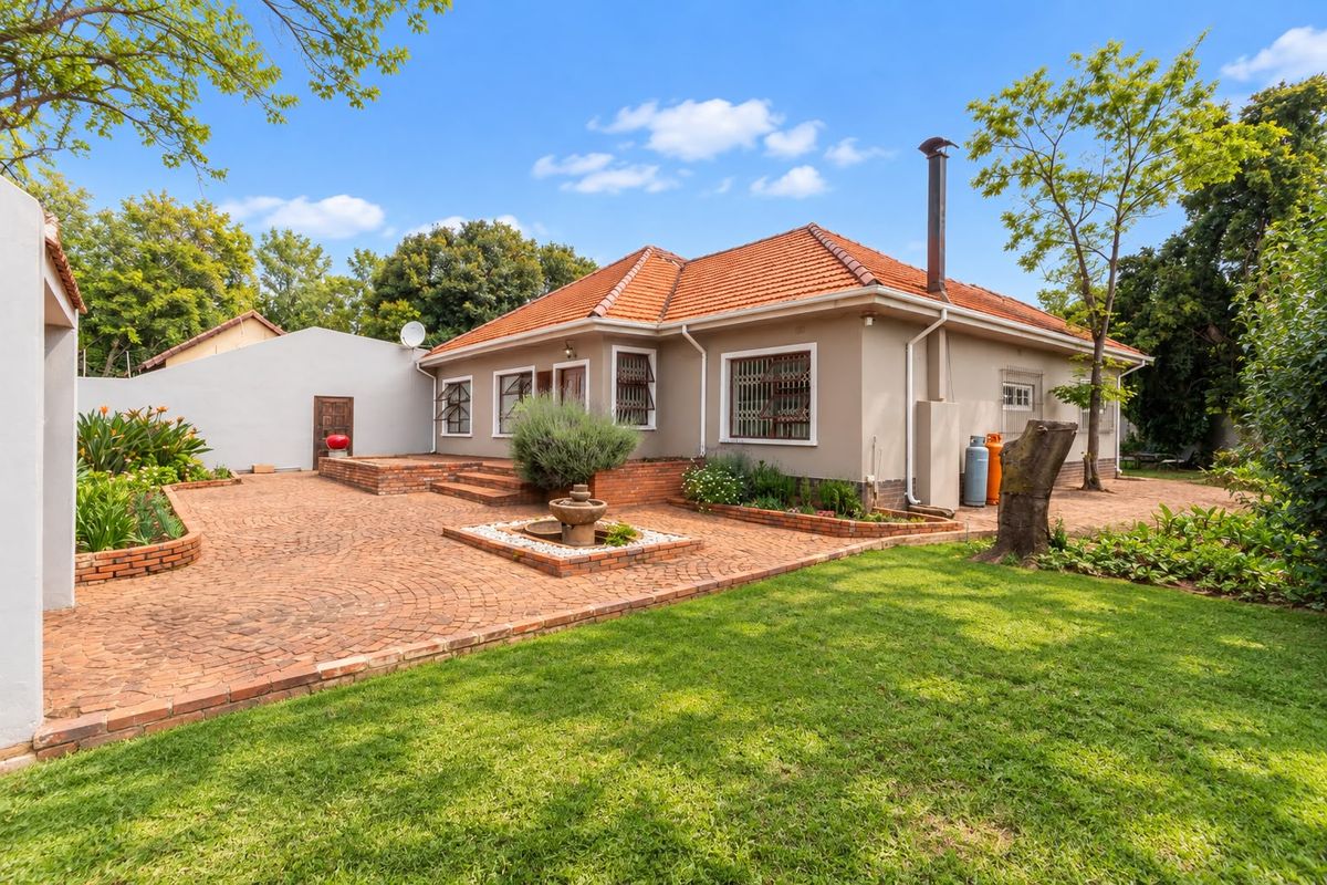 Rear view of the house featuring a terracotta tiled roof, extensive brick paved patio area, and a well-maintained garden with established landscaping.