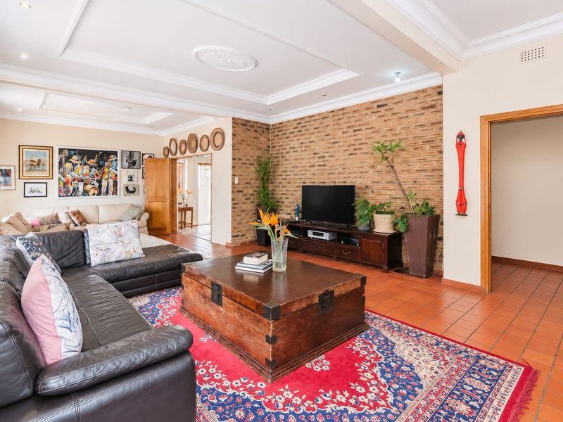 Spacious living room featuring a prominent exposed brick wall, recessed ceiling details, and durable terracotta tile flooring, offering a warm and inviting atmosphere.