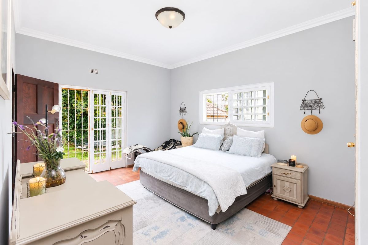 Spacious bedroom featuring terracotta tile flooring, crown molding, and direct access to the garden through classic French doors with security bars.