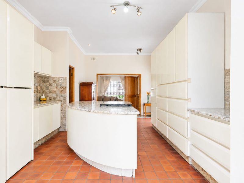 Spacious kitchen featuring ample built-in cabinetry, granite countertops with an integrated cooktop, and traditional terracotta floor tiles.