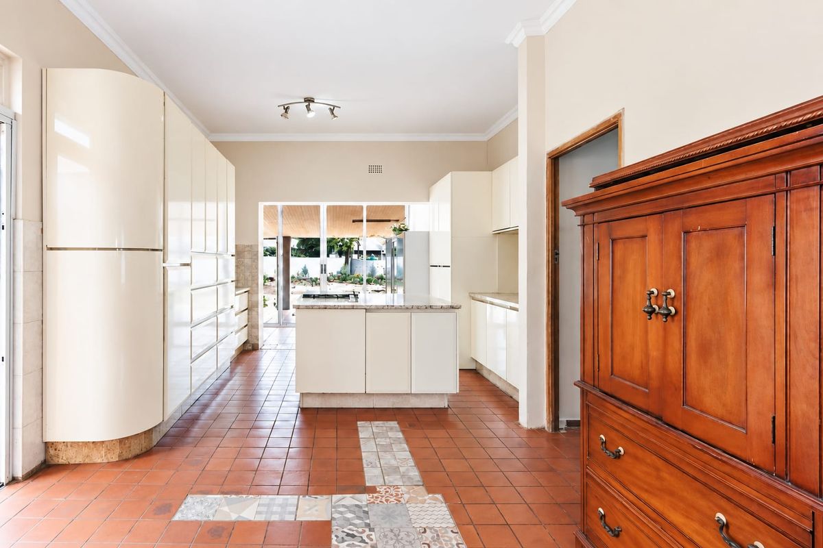 Spacious kitchen featuring high-gloss cabinetry, a central island with a gas hob, and terracotta tiled flooring with decorative inlay accents.
