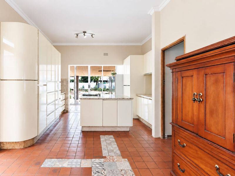 Spacious kitchen featuring high-gloss cabinetry, a central island with a gas hob, and terracotta tiled flooring with decorative inlay accents.