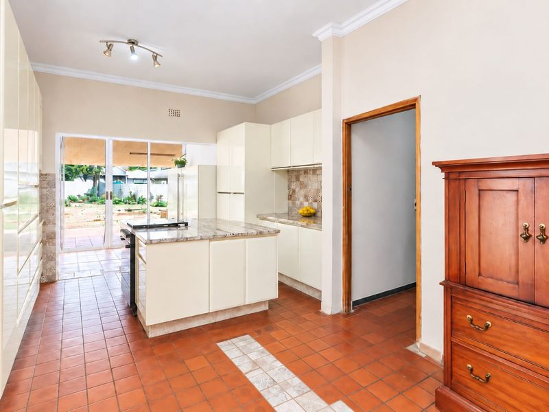A functional kitchen featuring cream cabinetry, stone countertops, a central island, and ceramic tile flooring with direct access to the rear patio.