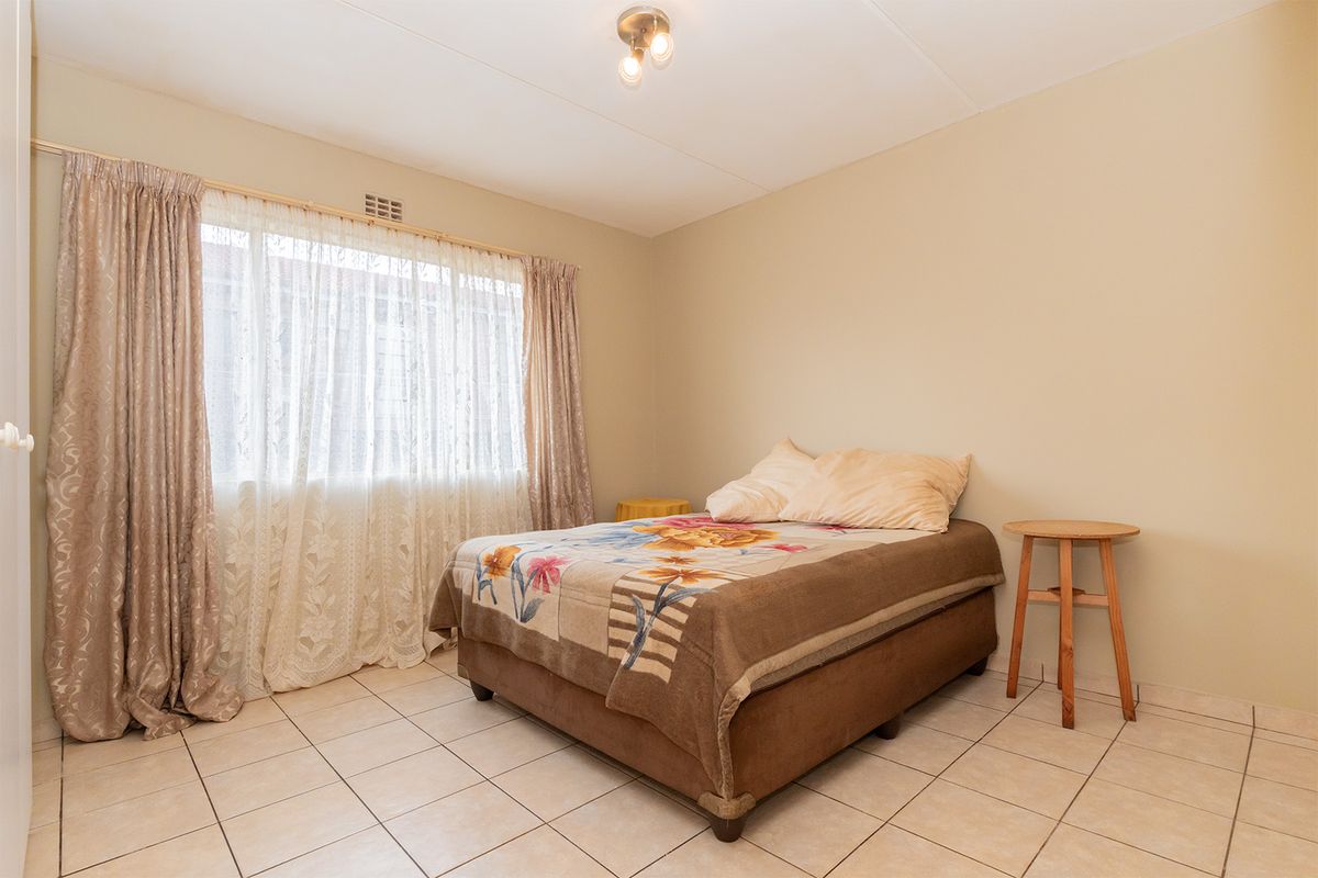 A functional bedroom featuring neutral wall tones, tiled flooring, and a large window that allows for natural light.