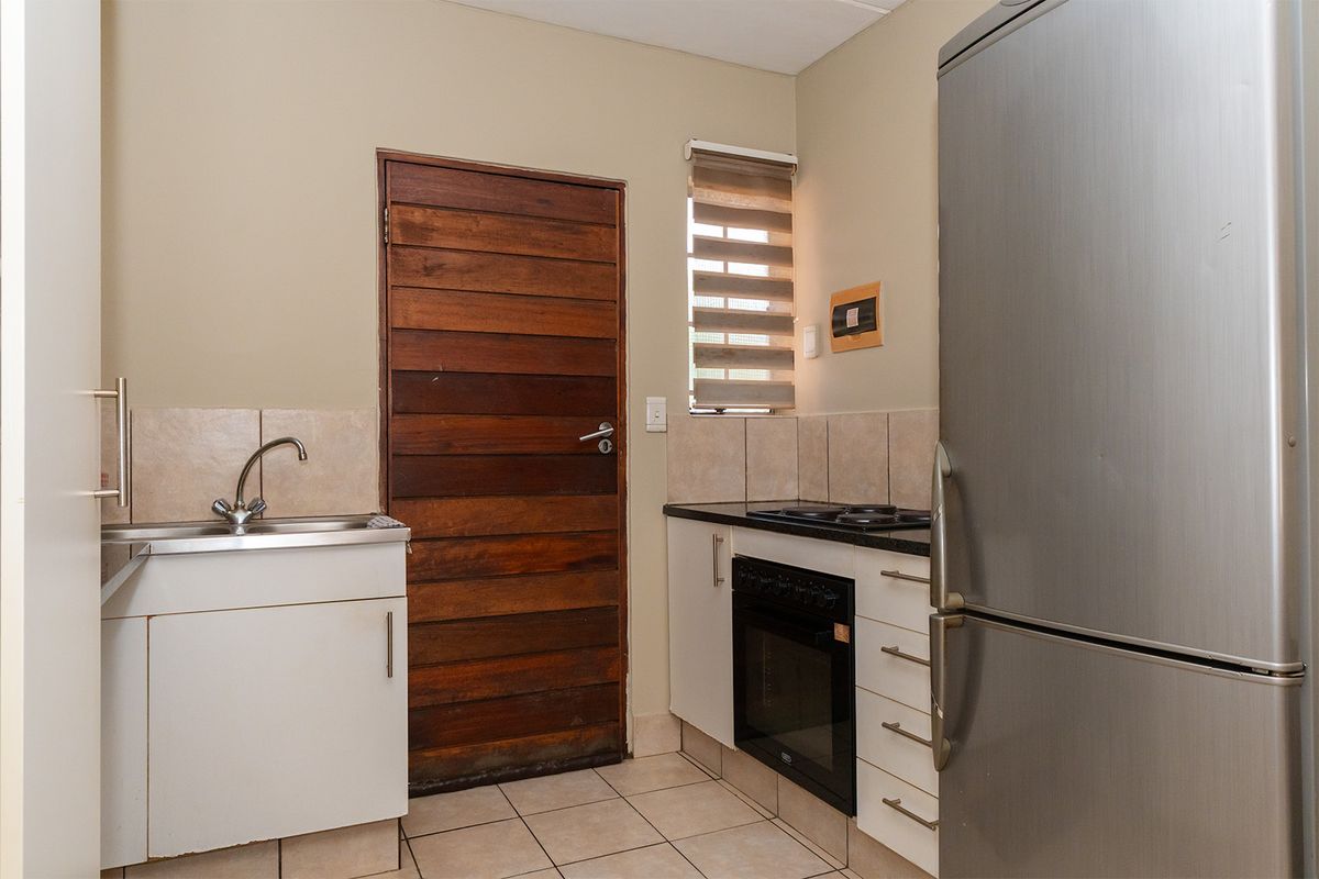 Compact kitchen featuring a built-in oven, electric hob, stainless steel sink, tiled backsplash, and tiled flooring.