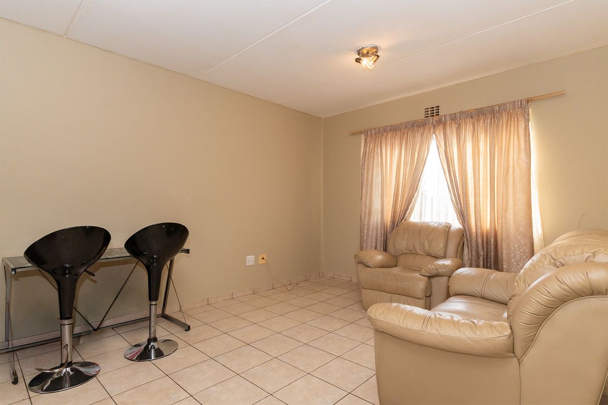 A living room featuring neutral wall paint, tiled flooring, and a window with curtain rod, providing a functional and versatile living space.
