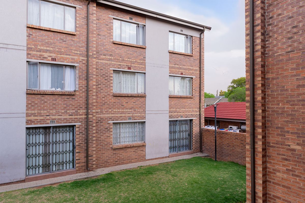 Rear view of a multi-story apartment building featuring face brick exterior, sliding security gates, and a small private lawn area.