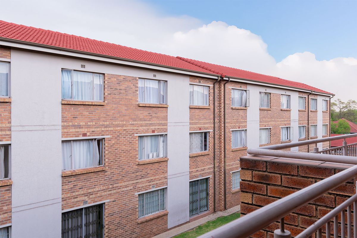 Exterior view of a multi-story apartment building featuring a brick facade, tiled roof, and metal balcony railings.