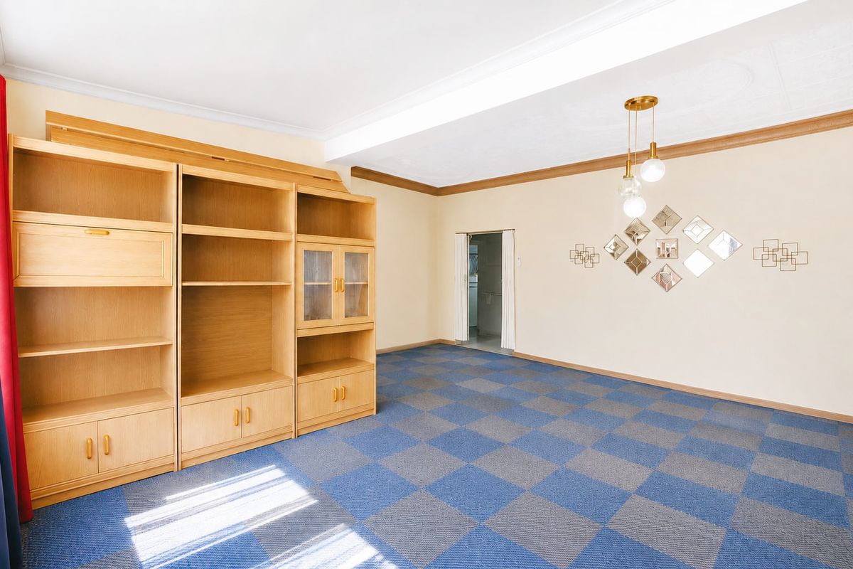 A living room featuring a large built-in wooden shelving unit, patterned carpet tiles, and decorative ceiling coving.