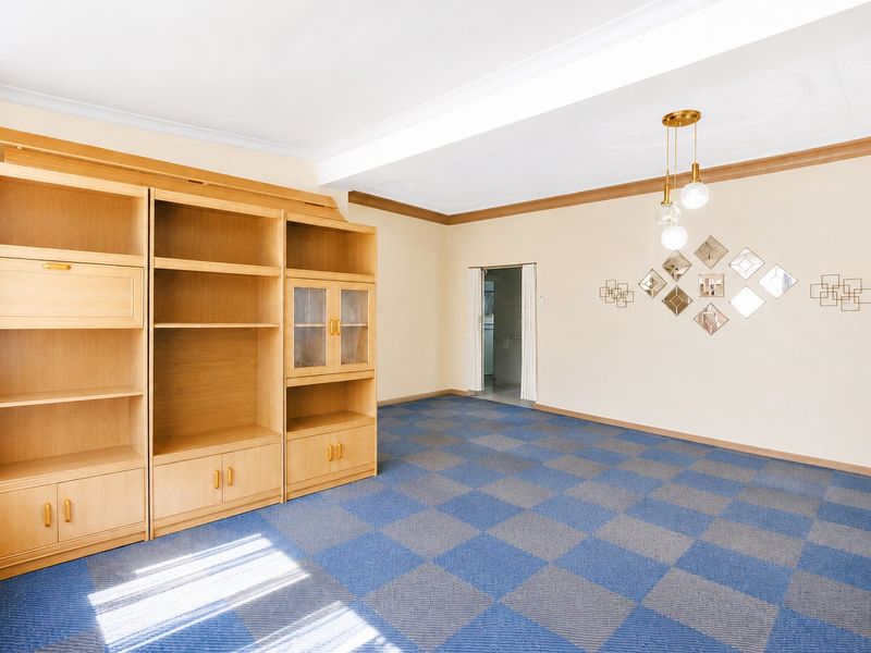 A living room featuring a large built-in wooden shelving unit, patterned carpet tiles, and decorative ceiling coving.