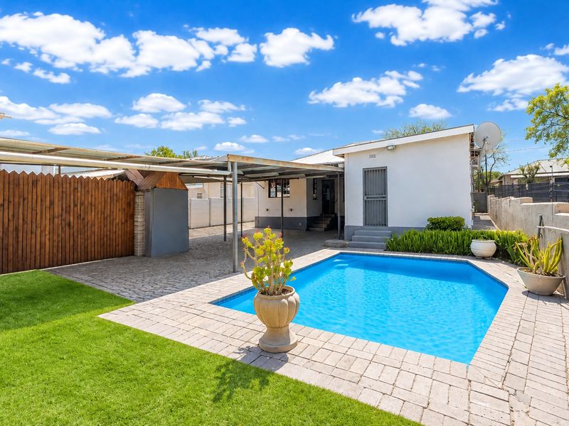 A well-maintained outdoor area featuring a swimming pool, paved surround, and a covered carport structure adjacent to the rear of the house.