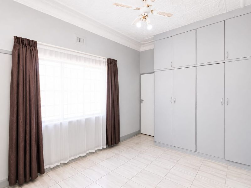 A bright, empty bedroom featuring neutral tiled flooring, built-in cupboards, and a ceiling fan, offering a clean and versatile space.