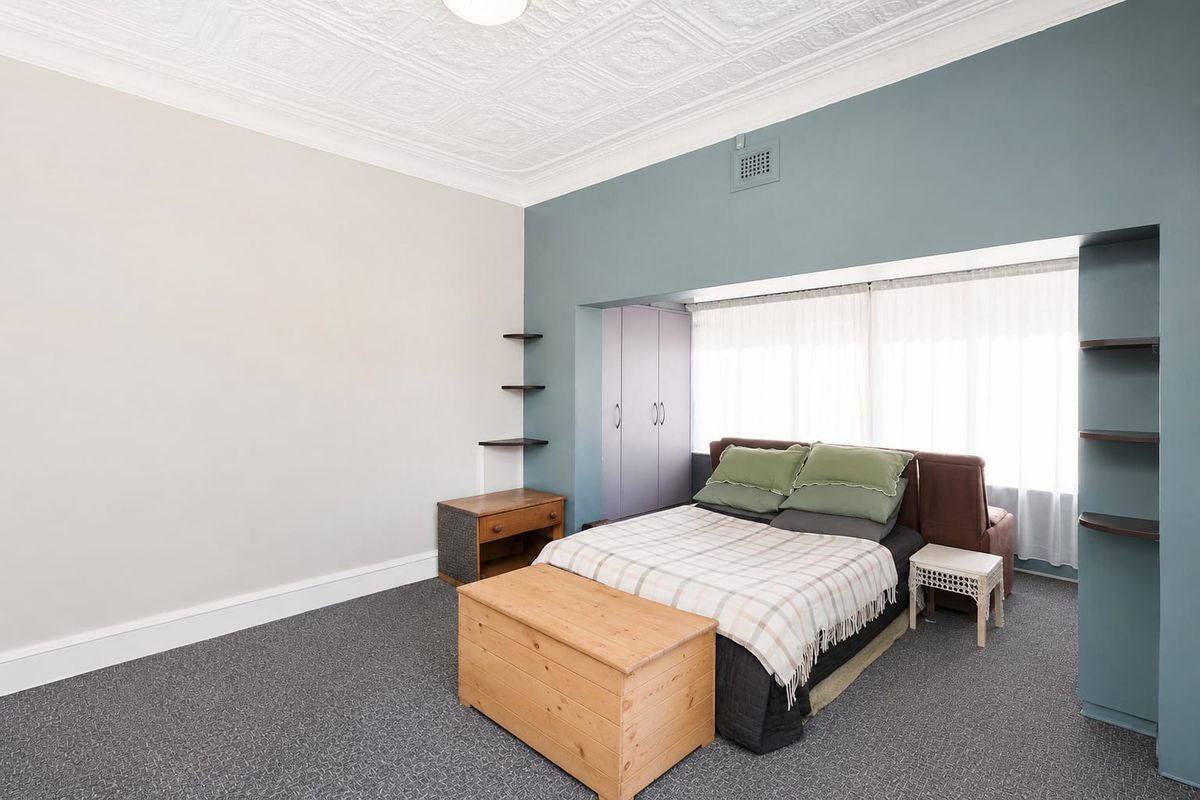 Spacious bedroom featuring a decorative ceiling, built-in wardrobe, and floating shelving, offering a comfortable and functional living space.