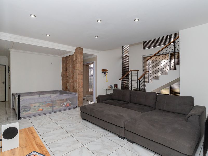 Spacious living area featuring modern tiled flooring, a distinctive stone feature pillar, and an open staircase with contemporary metal railings.