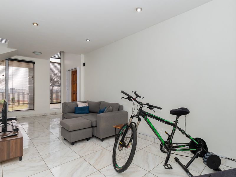 A bright living room featuring modern tiled flooring, recessed downlighting, and large windows with vertical blinds, offering a clean and neutral living space.