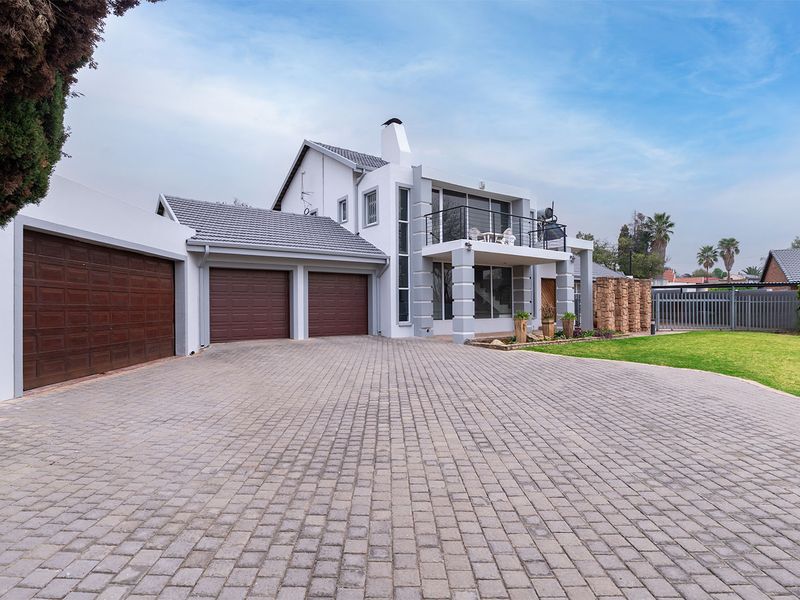 A well-maintained double-story residence featuring a spacious paved driveway, triple garage, and an upper-level balcony with modern architectural detailing.