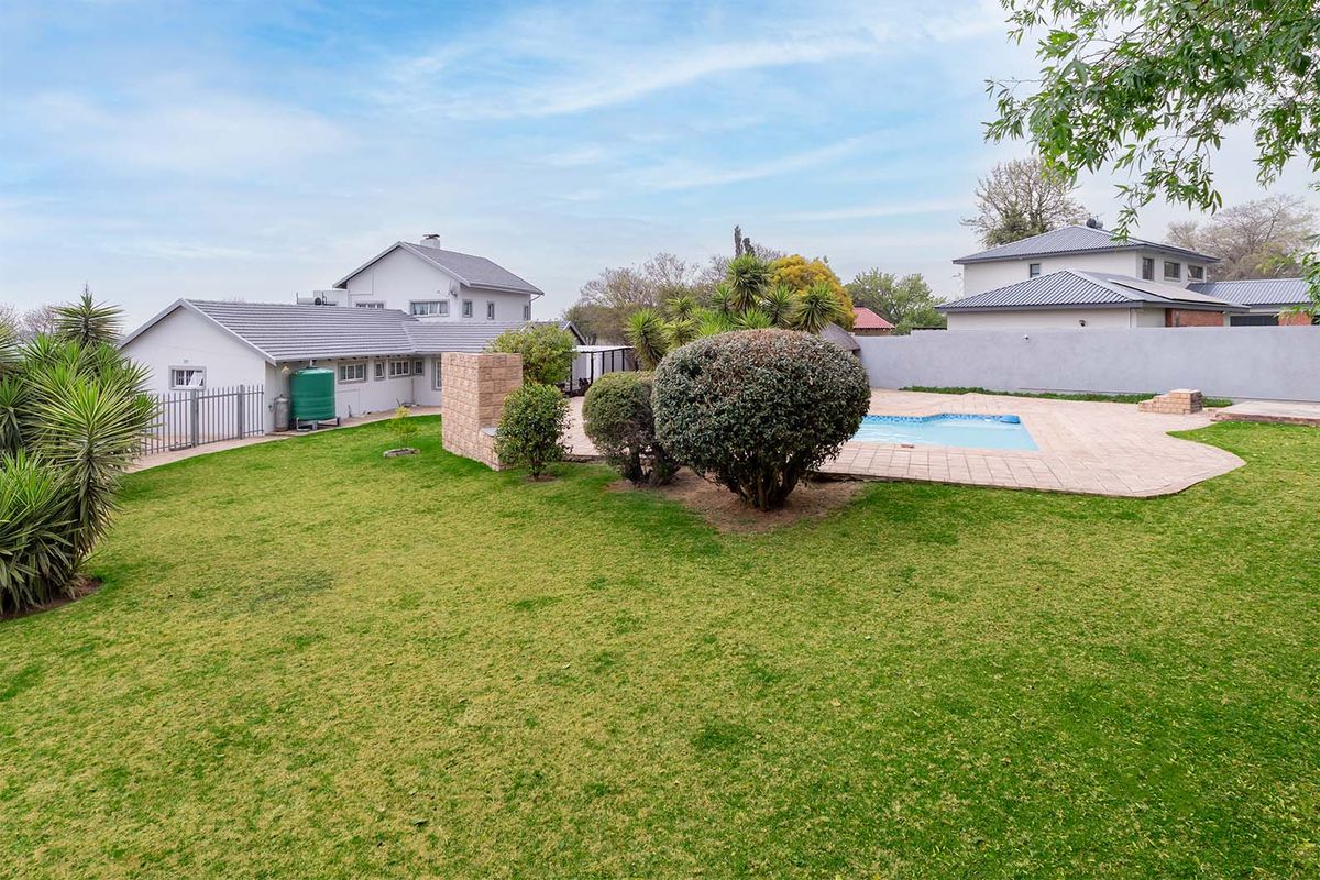 Spacious rear garden featuring a swimming pool with paved surround, built-in braai area, and a water tank, set against the rear elevation of the house.