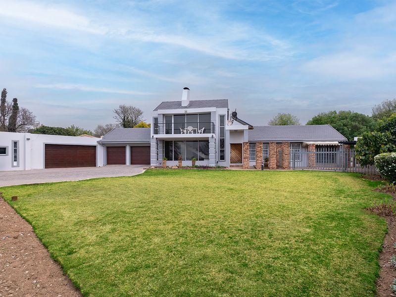 A well-maintained double-story residential property featuring a triple garage, stone-clad accents, a front balcony, and a spacious paved driveway with a manicured lawn.