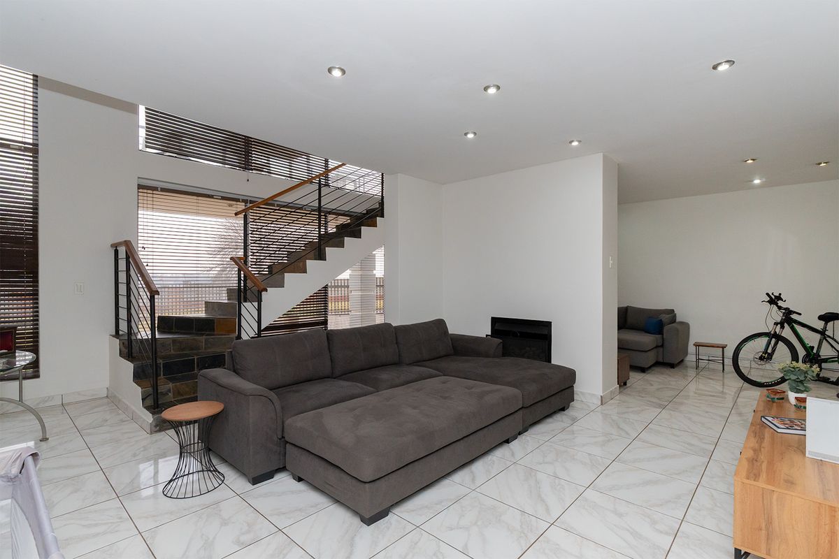 Spacious open-plan living area featuring modern tiled flooring, a built-in fireplace, and a striking staircase with a metal balustrade.