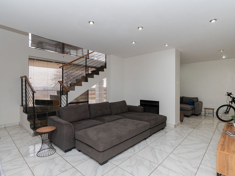 Spacious open-plan living area featuring modern tiled flooring, a built-in fireplace, and a striking staircase with a metal balustrade.