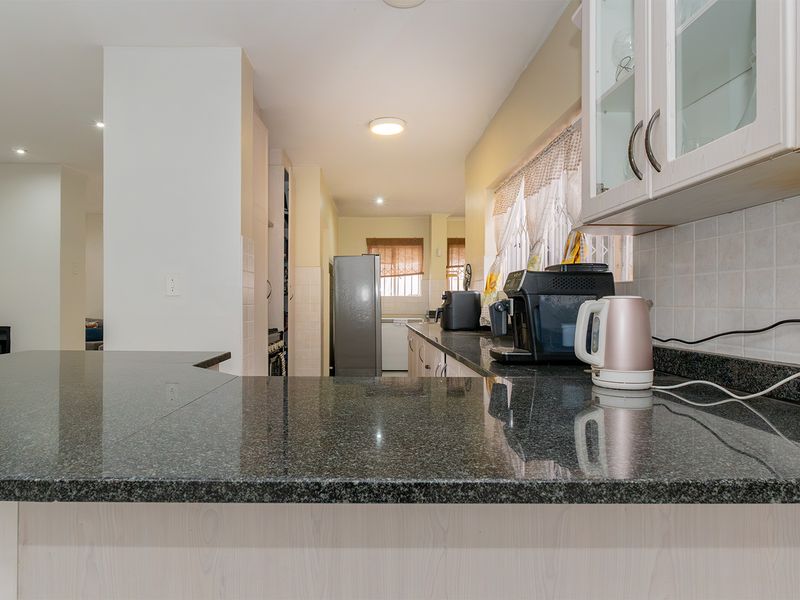 A functional kitchen featuring granite countertops, ample built-in cabinetry, and a tiled backsplash, offering a practical layout for daily meal preparation.