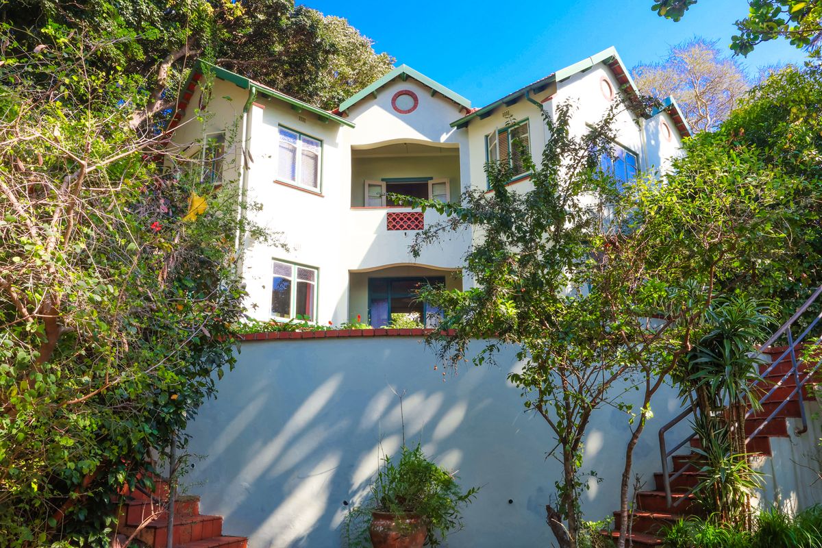 A multi-level residential exterior featuring a prominent retaining wall, external staircase, and balcony, set within a lush, mature garden environment.