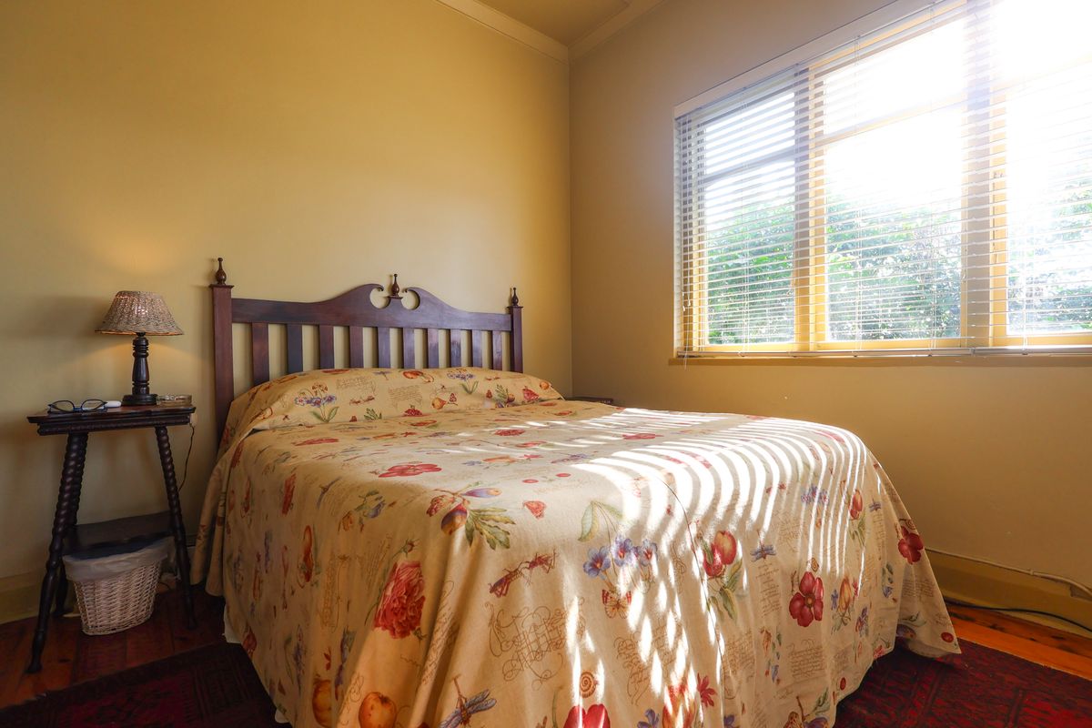 A cozy bedroom featuring warm-toned walls, timber flooring, and natural light filtered through venetian blinds.