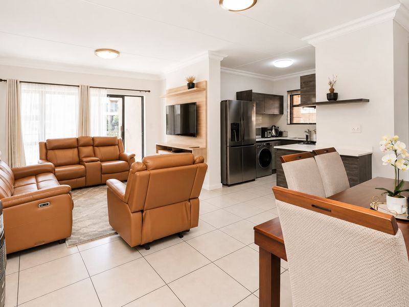 Spacious open-plan living and dining area featuring tiled floors, modern kitchen cabinetry with stone countertops, and seamless access to an outdoor balcony.