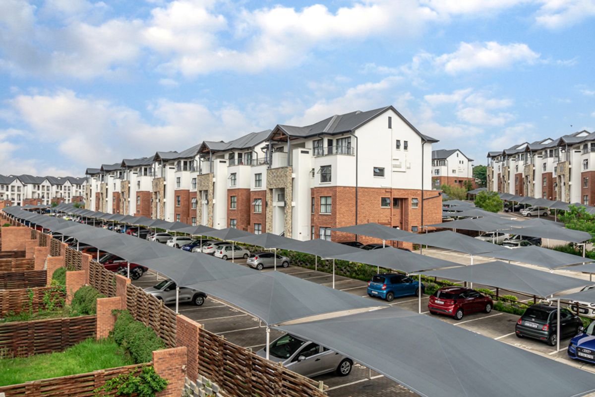 An elevated view of an apartment complex featuring extensive paved parking areas with shade cloth carports and well-maintained brick and timber boundary structures.