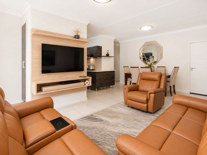 Modern open-plan living and dining area featuring tiled floors, a custom built-in media unit, and a seamless transition to the kitchen space.