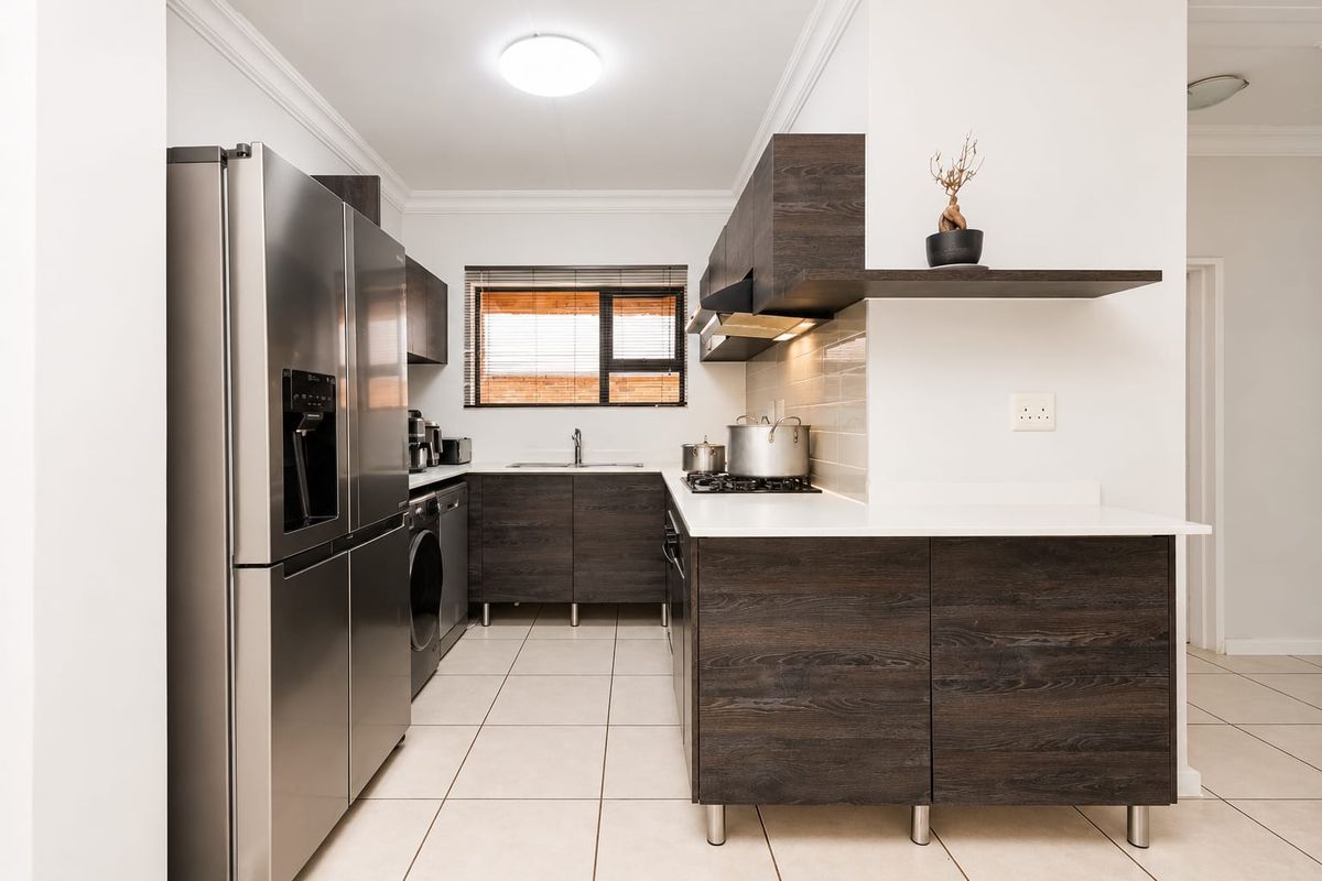 Modern kitchen featuring dark wood cabinetry, white stone countertops, gas hob, extractor fan, and tiled flooring in a clean, functional layout.