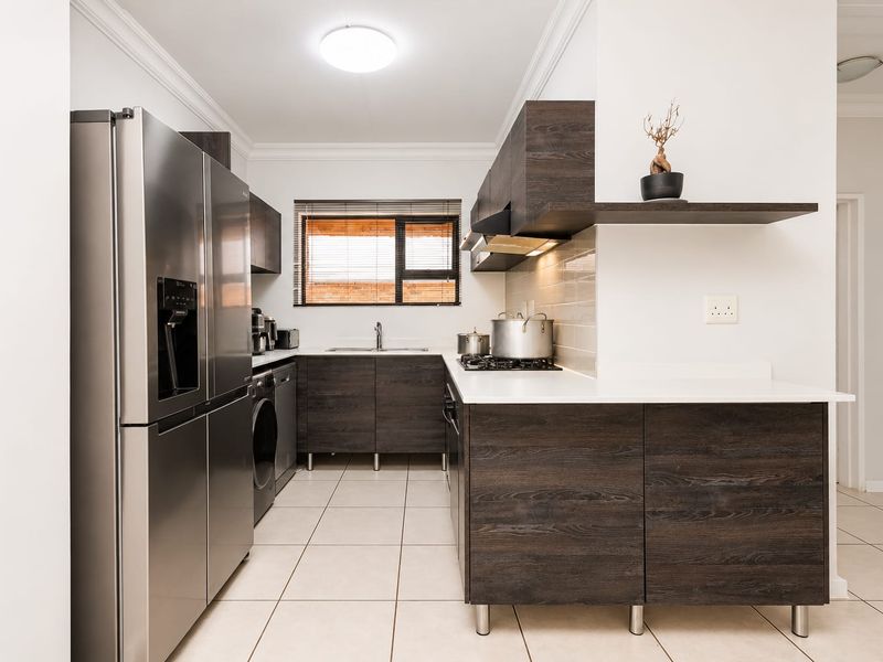 Modern kitchen featuring dark wood cabinetry, white stone countertops, gas hob, extractor fan, and tiled flooring in a clean, functional layout.