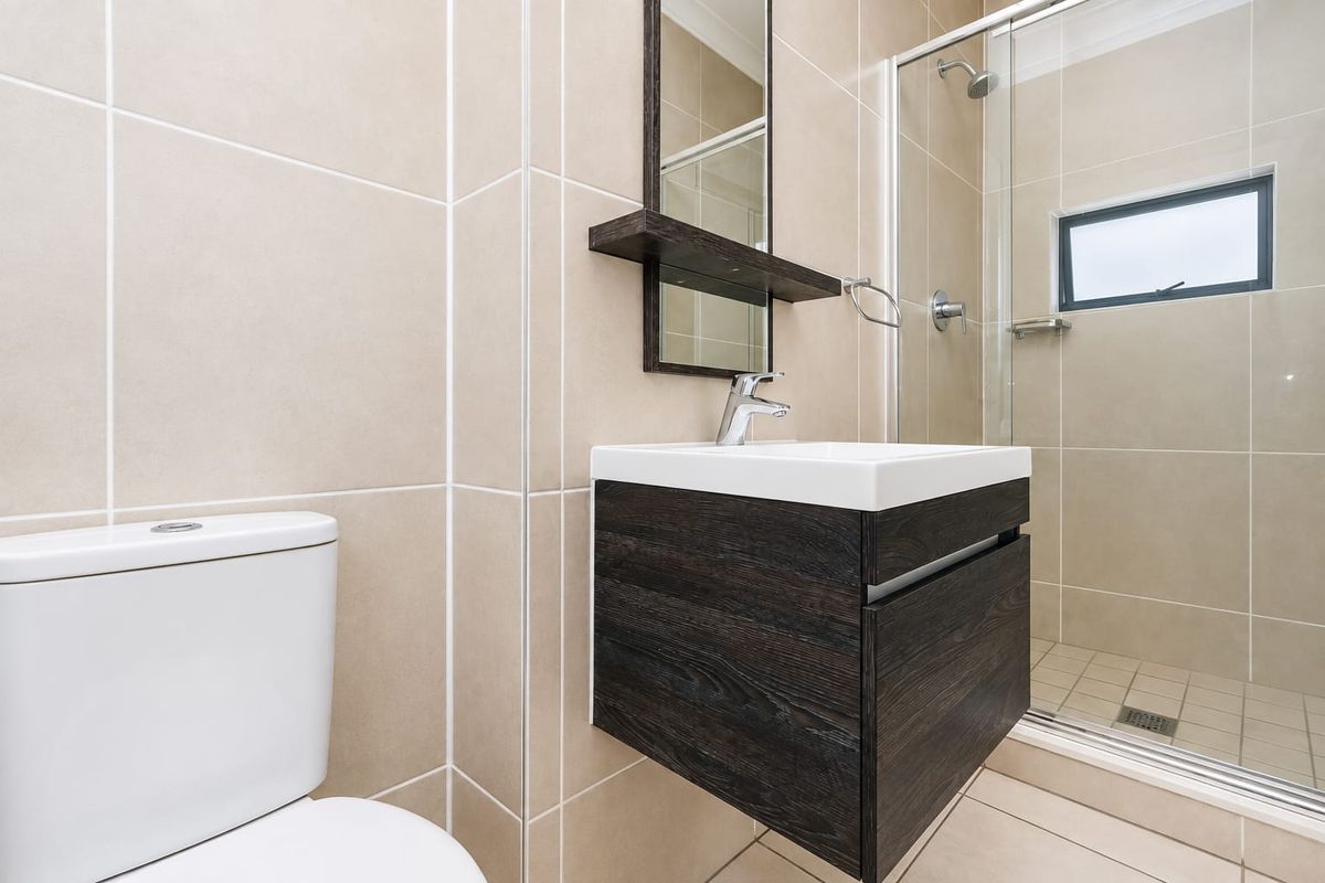 Modern bathroom featuring a wall-mounted vanity, glass-enclosed shower, and neutral floor-to-ceiling tiling.