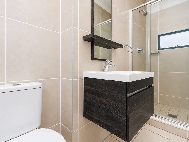Modern bathroom featuring a wall-mounted vanity, glass-enclosed shower, and neutral floor-to-ceiling tiling.