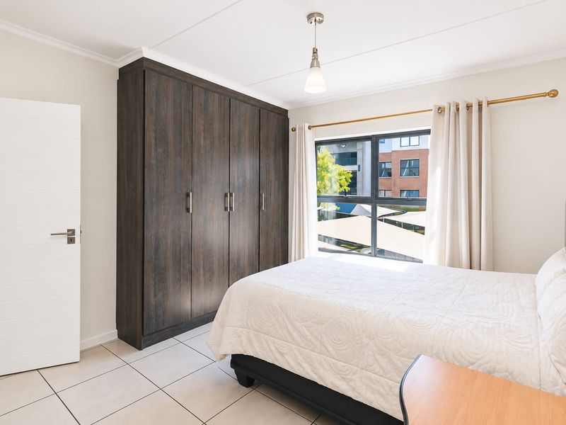 A well-maintained bedroom featuring neutral tiled flooring, a large dark wood built-in wardrobe, and a window providing natural light.