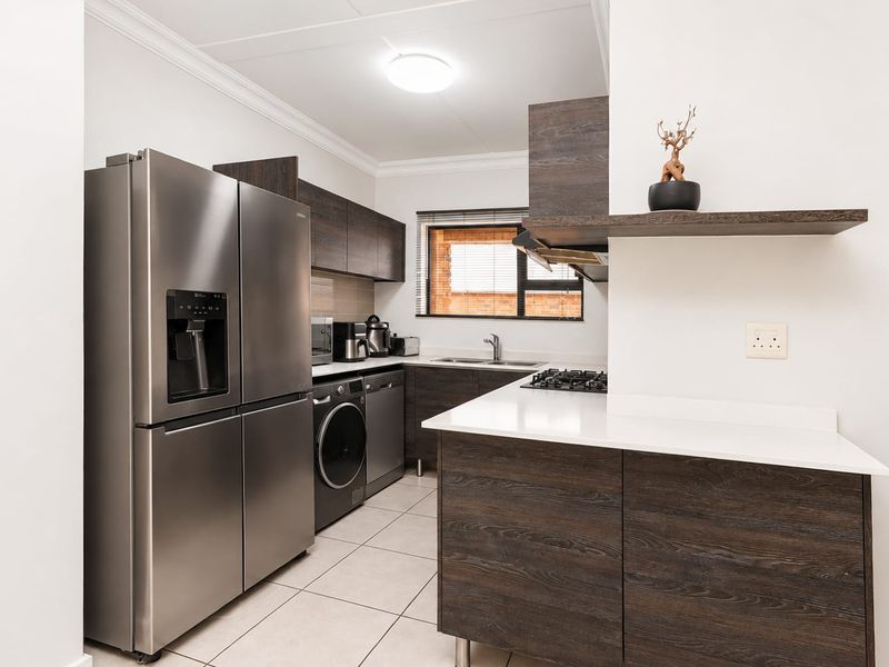 Modern kitchen featuring dark wood cabinetry, stone countertops, a gas hob, and integrated laundry appliances, finished with neutral floor tiles.
