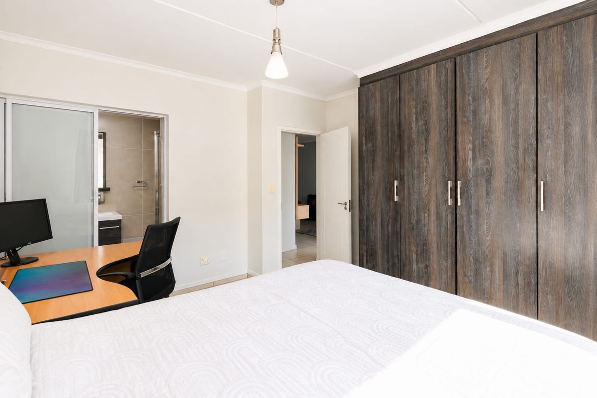 A well-maintained bedroom featuring extensive built-in wooden cupboards, a pendant light, and direct access to an en-suite bathroom.