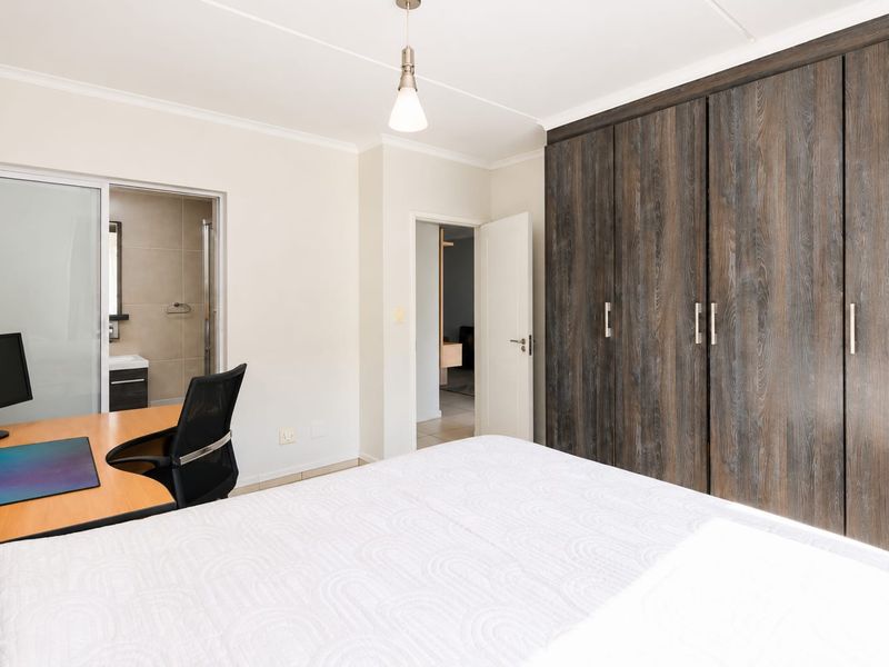 A well-maintained bedroom featuring extensive built-in wooden cupboards, a pendant light, and direct access to an en-suite bathroom.