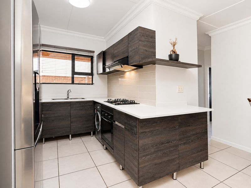 Modern kitchen featuring dark wood-grain cabinetry, stone countertops, gas hob, integrated oven, and tiled flooring in a clean, well-maintained layout.