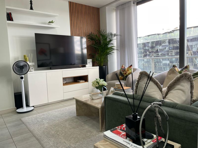 Modern living room featuring stylish slatted wood wall paneling, built-in floating shelves, and large floor-to-ceiling windows providing ample natural light.